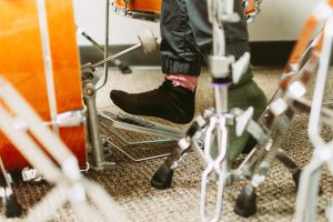 Close-up of a small foot in a black sock on a bass drum pedal behind an orange drum kit.