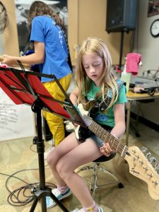 8 year-old, female with long blond hair is sitting on a chair playing electric guitar.