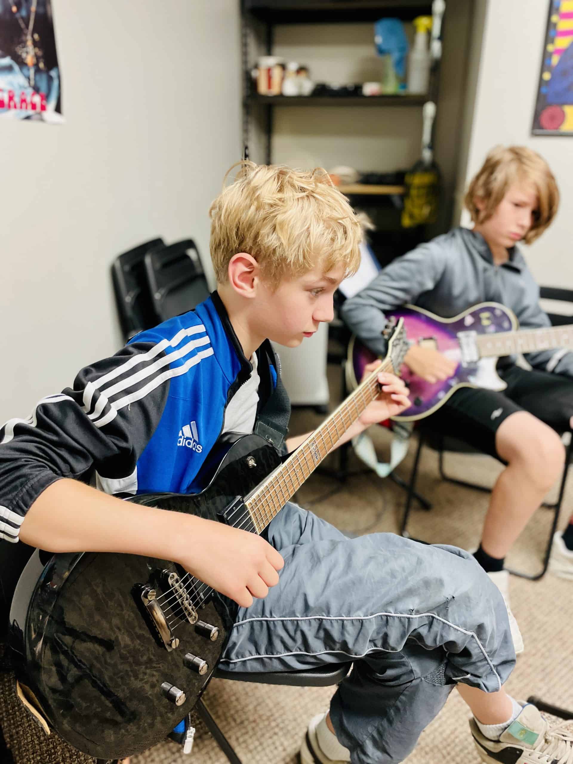 10 year-old male with short blonde hair is sitting on chair and playing electric guitar.