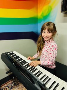9 year-old female with long brown hair in a side ponytail is playing a keyboard.