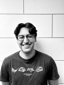 Black and white photo of a young adult male with short black hair and glasses.