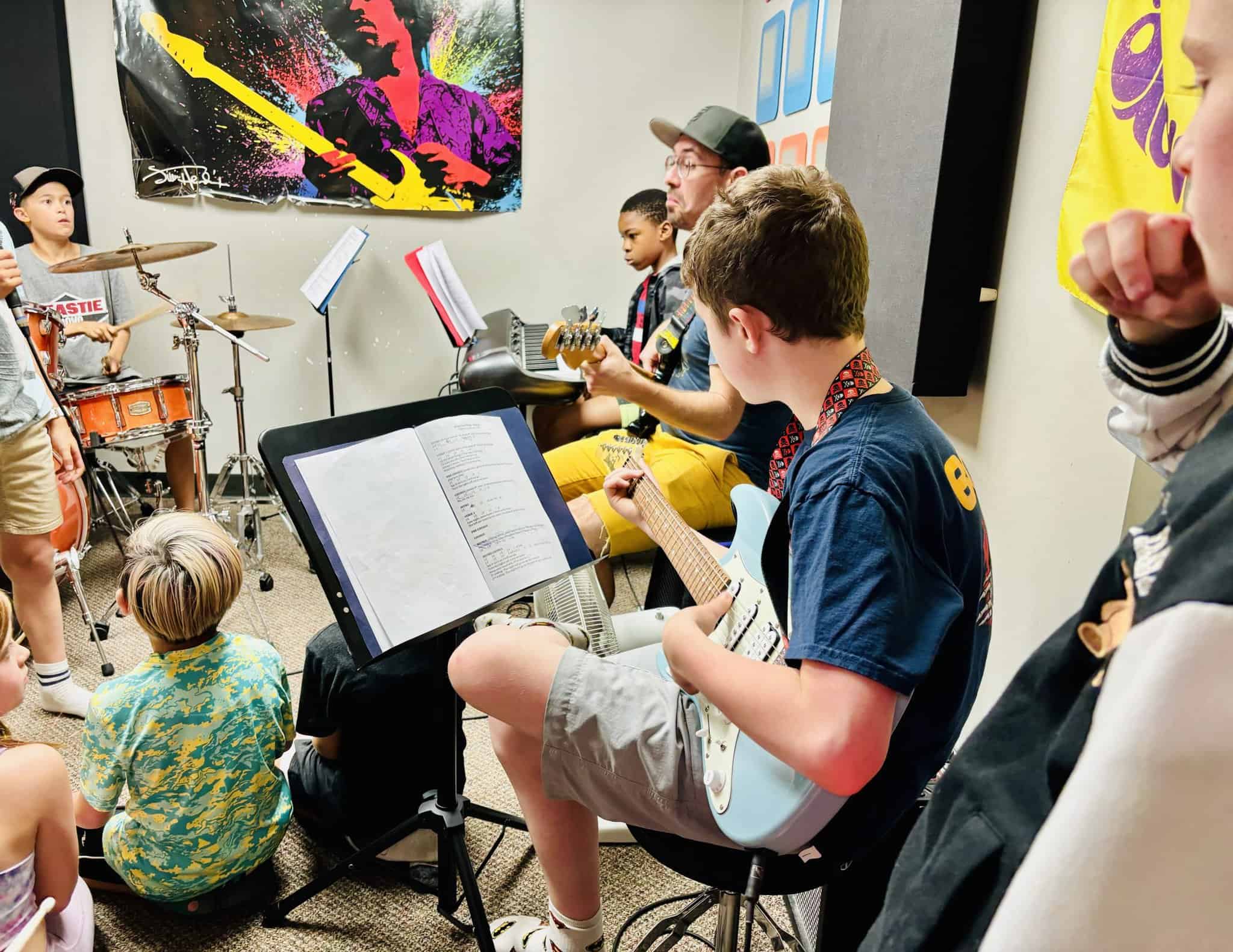 Group Music Class Summer 2024 A group of nine and ten year old kids playing electric guitar, keyboards and drums under the direction of a teacher.