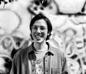 Donovan Lane. Black and white photo. Donovan has short, dark hair. He's wearing metal-rimmed glasses and is smiling.