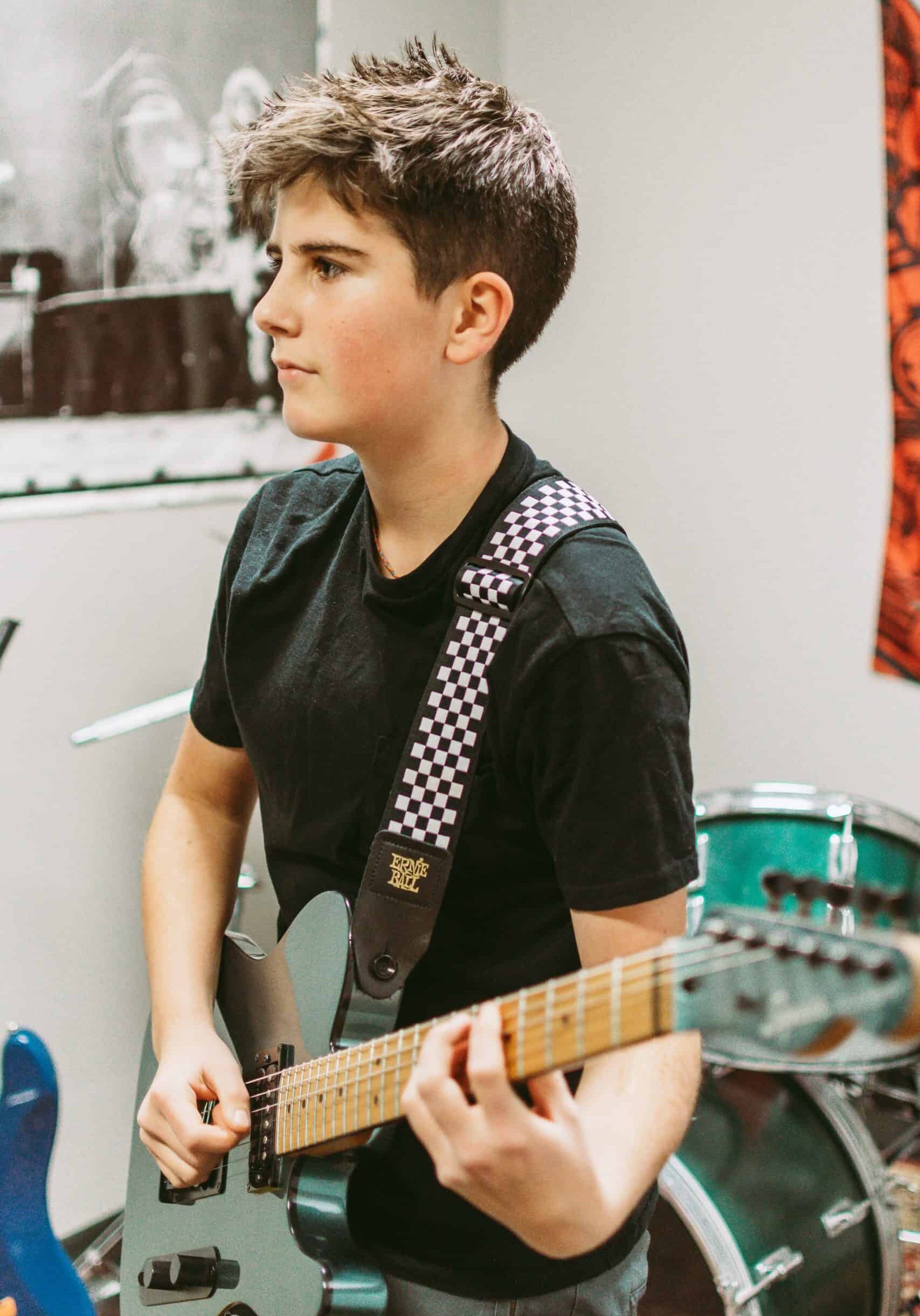 Stella Leo taking guitar lessons at Backbeat. 12 year-old boy with spikey, dark brown hair plays a seafoam green electric guitar.