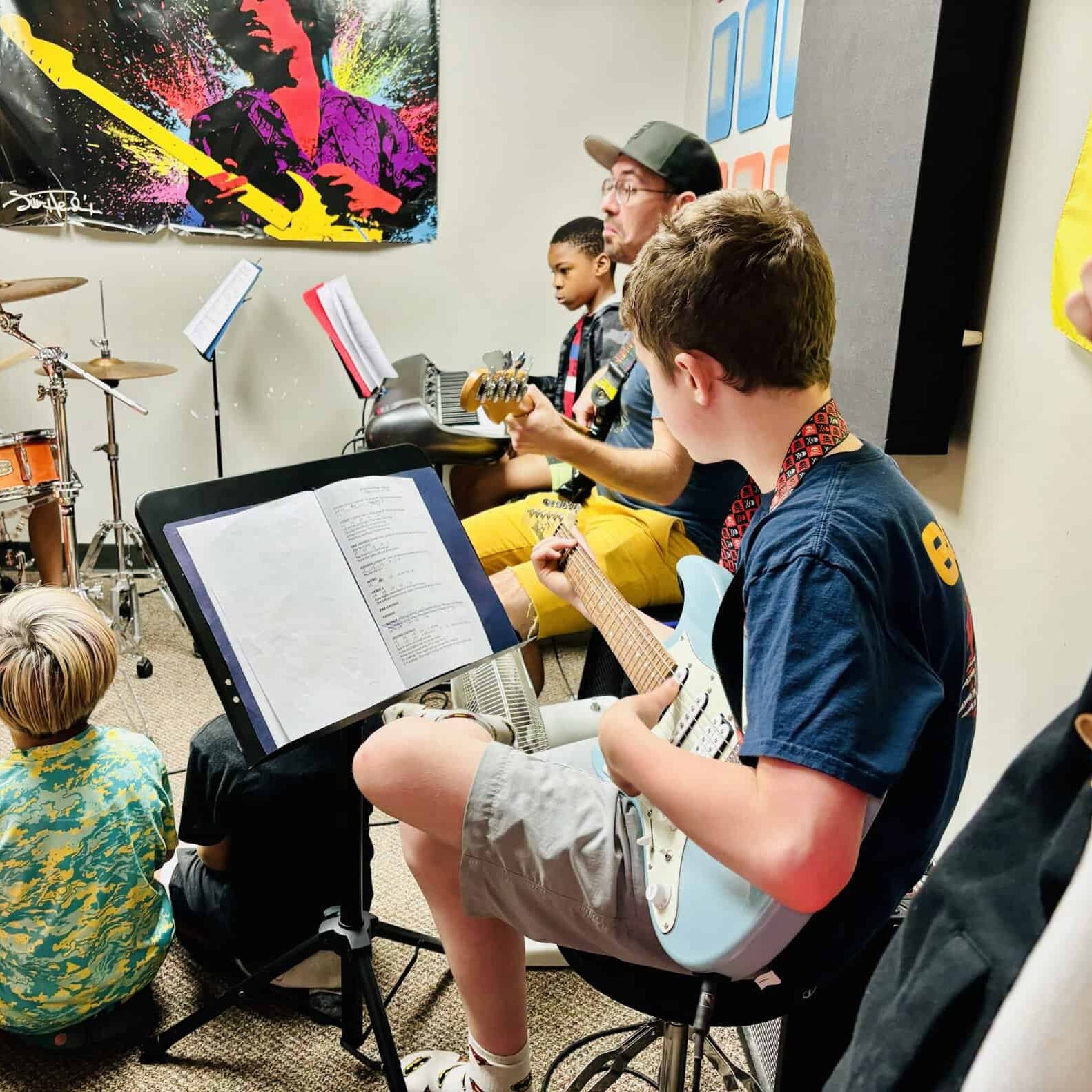 Group Music Class Summer 2024 A group of nine and ten year old kids playing electric guitar, keyboards and drums under the direction of a teacher.